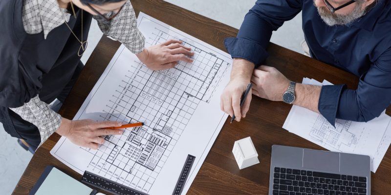 High angle view of two engineers examining project of new building at the table at office