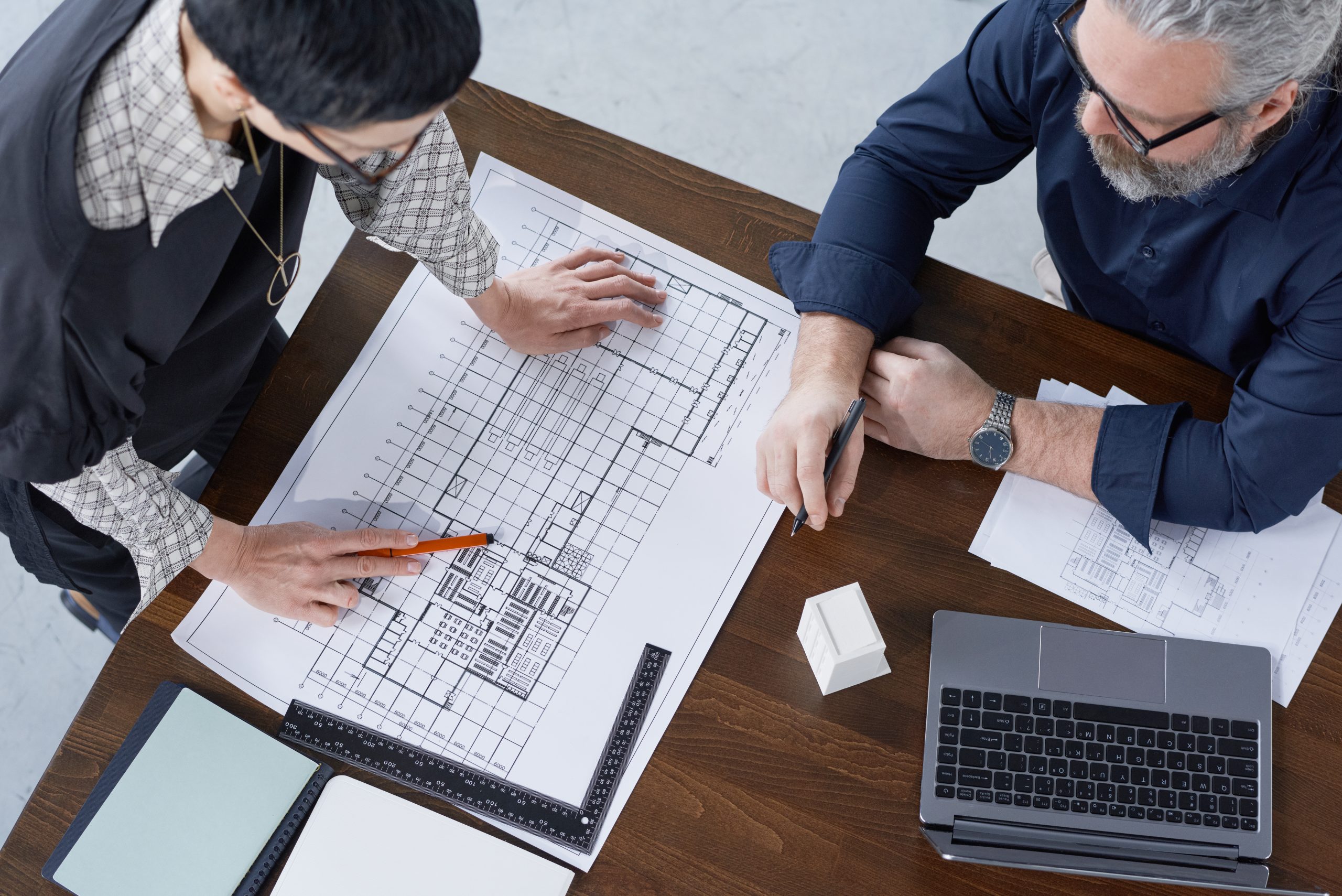 High angle view of two engineers examining project of new building at the table at office